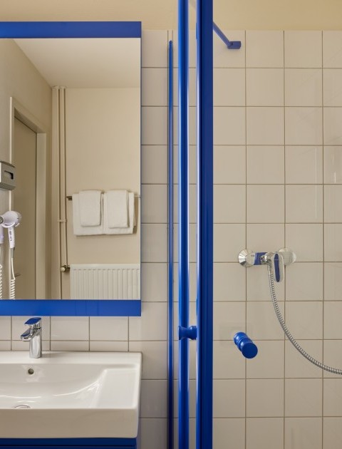 Modernes Bad mit einem beleuchteten Spiegel, Waschbecken, Föhn und einer Dusche mit Handbrause und einem Seifenspender