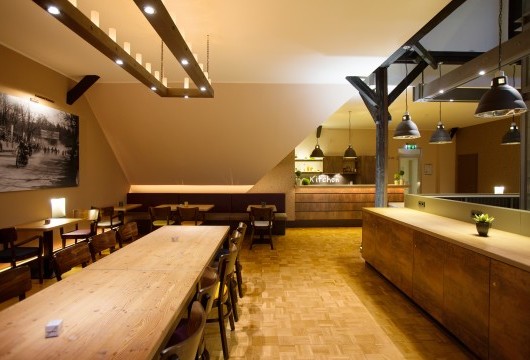 Ein einladender Essbereich mit stilvoller Beleuchtung in der Talking Kitchen Hannover, mit hölzernen Tischen und Stühlen