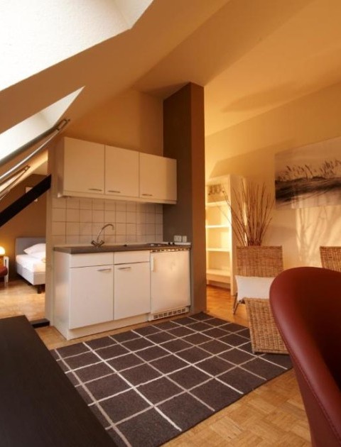 Gemütliches Apartment unter dem Dach mit einer Küchenzeile, einem Arbeitsbereich, Sessel und Schlafbereich im Hintergrund