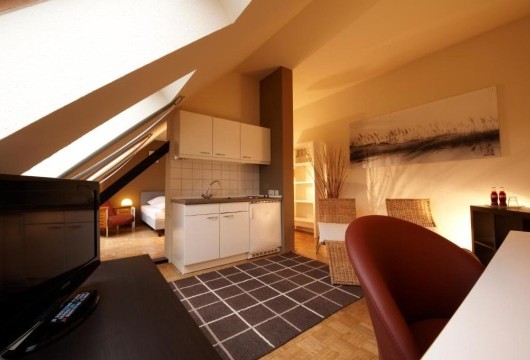 Gemütliches Apartment unter dem Dach mit einer Küchenzeile, einem Arbeitsbereich, Sessel und Schlafbereich im Hintergrund