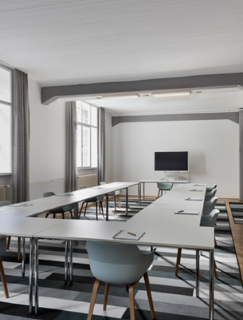 Heller Seminarraum in Hannover, mit U-förmiger Bestuhlung, einem TV-Bildschirm, großen Fenstern und einer Tafel an der Wand