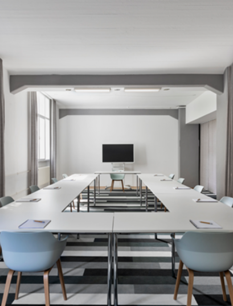 Heller Seminarraum in Hannover, mit U-förmiger Bestuhlung, TV-Bildschirm, großen Fenstern und Tafel an der Wand